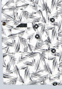 Weißes Hemd mit einem schwarzen, eckigen geometrischen Muster, ausgestattet mit sechs schwarzen Knöpfen und einem schwarzen Taschen-Detail auf der linken Seite.