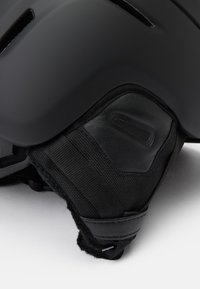 Schwarzer Helm mit matter Oberfläche, ausgestattet mit Belüftungsöffnungen, gepolstert mit strukturiertem Stoff und einem glatten Lederakzent am Kinnriemen.