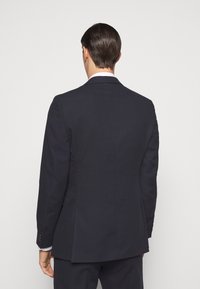 Marineblazer mit maßgeschneidertem Design, einzelner Schitz und drei-Knopf-Manschetten, aus glattem Stoff und mit strukturierter Silhouette.