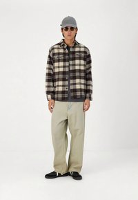 Pledinė juoda ir kreminė marškinėliai, derinami su šviesiais smėlio spalvos platėjusių kelnių. Aksesuarai: pilka kepuraitė ir tamsūs akiniai nuo saulės, juodi sportbačiai.