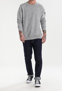 Sudadera gris de manga larga con una textura sutil, combinada con jeans de mezclilla azul oscuro y zapatillas negras con suelas blancas y puños doblados.