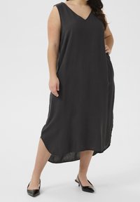 Femme portant une robe noire midi sans manches avec un décolleté en V et un ourlet incurvé, associée à des escarpins slingback noirs à bout pointu.