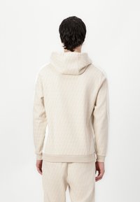 Felpa con cappuccio beige con un motivo di foglie testurizzato, polsini e orlo a coste, e accenti laterali bianchi a contrasto. Realizzata in un tessuto morbido.