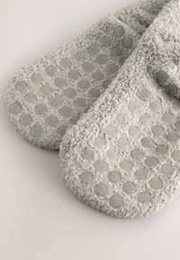 Szare teksturowane kapcie z puszystym wykończeniem i gumowymi, kropkowanymi nakładkami na podeszwach dla lepszej przyczepności. Zaokrąglony nosek i miękki, pluszowy wygląd.