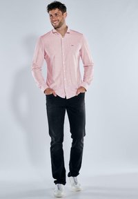 Langärmliges Rot- und Weiß gestreiftes Hemd mit Knopfverschluss, kombiniert mit schwarzen Hosen und weißen Schuhen, im entspannenden Schnitt.