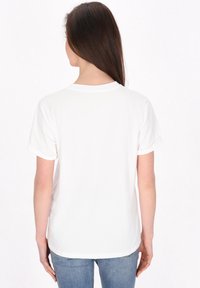 Hvid kortærmet t-shirt med rullede ærmer, rund halsudskæring og en glat tekstur, set fra ryggen, kombineret med blå jeans.