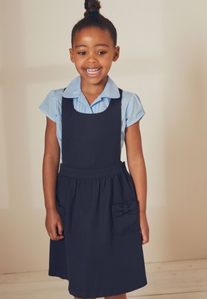 Abito blu navy con corpetto aderente e gonna svasata. Presenta una tasca con un'accento a fiocco. Camicia azzurra chiara con colletto sotto.