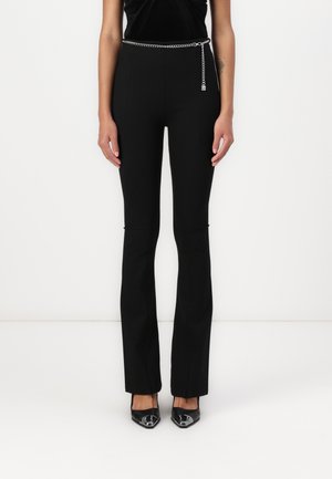 Black tailored pants with a flared design, featuring a silver chain belt and a smooth texture. Paired with pointed black shoes.