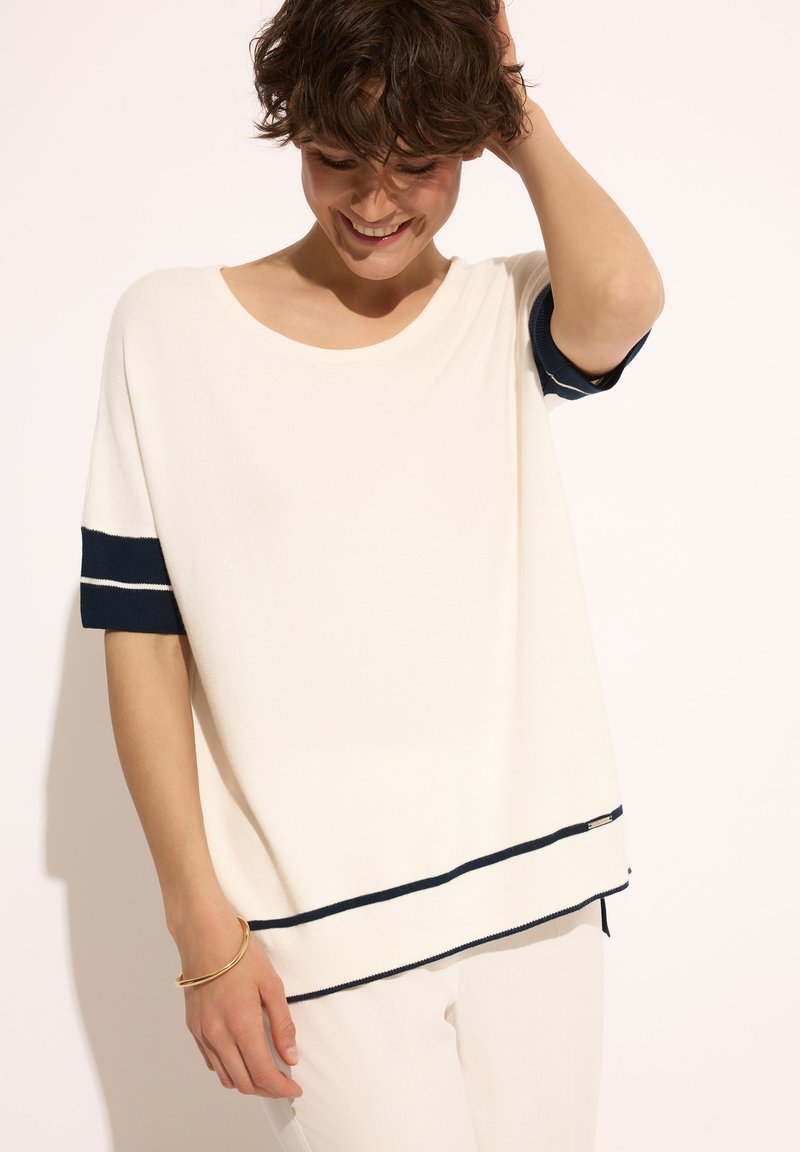 Biała bluzka z krótkim rękawem, z granatowymi paskami na rękawach i dolnym brzegu, z okrągłym dekoltem i miękkim, teksturowanym materiałem. Minimalistyczne detale designu.