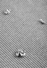 Élément décoratif en ton argenté avec trois cristaux en forme de goutte d'eau sur un fond gris texturé à rayures.