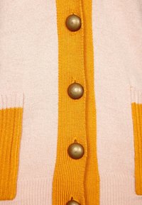 Stickad kavaj i rosa och gult, med en knappad front med guldfärgade knappar och kontrasterande ribbad textur på kanterna och fickorna.