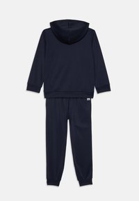 Tamsiai mėlynas treniruoklių kostiumas su gobtuvu ir atitinkančiomis kelnėmis. Yra šonkauliniai rankogaliai ir liemuo, lygus audinys ir logotipas liemenyje.