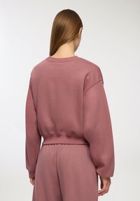 Felpa a maniche lunghe aderente in rosa polveroso, realizzata in un tessuto morbido con polsini e orlo a coste. La vista posteriore mostra un colletto liscio e un design pulito.