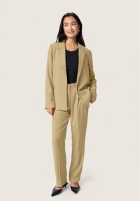 Beige suit consisting of a blazer and tailored pants, paired with a black ribbed top, completed with black pointed-toe heels.
