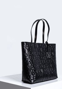 Černá taška tote z lesklé kůže s reliéfním vzorem loga. Má dvojité rukojeti a odnímatelný štítek jako akcent. Obdélníkový tvar.