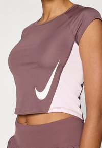 Καφέ και ροζ κοντό αθλητικό τοπ με λευκό λογότ υπο Nike, που διαθέτει κοντά μανίκια και λείο, ελαστικό ύφασμα.