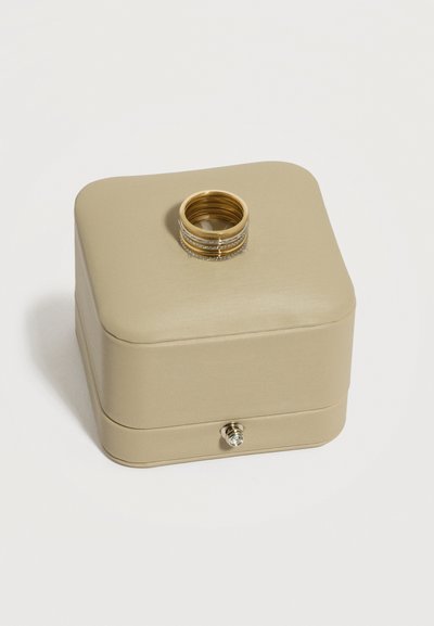 Zloženi zlati prstani z vgrajenimi majhnimi diamanti ležijo na zaprti bež usnjeni škatli za nakit s srebrnim zaponkom.