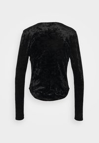 Svart långärmad skjorta i mjukt, textuerat sammetstyg. Har rundad nederkant och slät yta. Inga synliga knäppningar eller mönster.