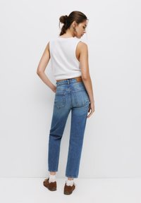 Höga ljusblå jeans med rak passform, sidofickor och en läderlapp vid midjan, tillsammans med en vit ärmlös topp.
