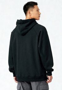 Felpa con cappuccio nera con una texture morbida, dotata di una tasca a marsupio, polsini a costine e un cappuccio. Sul retro presenta un design semplice con cuciture minime.