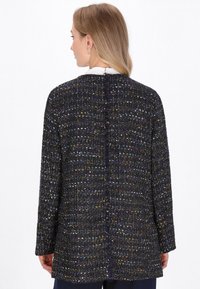 Giacca nera con texture e fili multicolori, caratterizzata da una vestibilità ampia, maniche lunghe e una cucitura posteriore dritta.