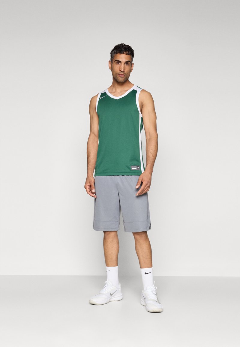 Groene sportieve mouwloze shirt met witte accenten, gecombineerd met grijze sportshorts. De outfit heeft een Nike-logo en een sportief ontwerp.