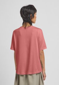 Kortebloemige, losse top van zachte koraalkleurige stof. Heeft een eenvoudige ronde hals en een naaddetail aan de achterkant.