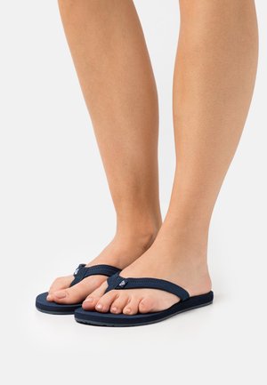 Flip-flops bleumarin cu bretele texturate, talpă plată și un mic accent cu logo. Material moale cu un design minimalist.