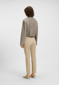 Gekürzte, hellbraune Jacke mit strukturiertem Finish und elastischem Bund, kombiniert mit beigen maßgeschneiderten Hosen und hellbraunen Absatzschuhen.