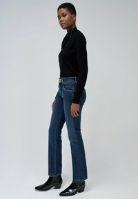 Top negro de manga larga con un cuello redondeado, combinado con unos jeans azules de cintura media y botas negras hasta el tobillo con tacón cuadrado. Diseño sencillo y ajustado.
