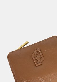 Portafoglio in pelle marrone con superficie texture, dotato di una zip dorata e di un logo impresso al centro. Forma rettangolare, design compatto.
