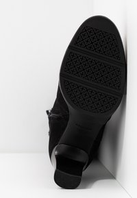 Stivale alla caviglia in suede nero con suola in gomma nera texturizzata, caratterizzato da un design elegante e una punta arrotondata. Nessun hardware o motivo prominente.