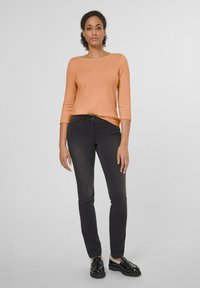 Oranje lange mouwen trui met een bootnek, gecombineerd met zwarte slim-fit jeans en zwarte schoenen, met een gladde textuur.