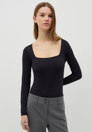 Body nero a maniche lunghe con scollo quadrato, realizzato in tessuto morbido ed elasticizzato; abbinato a pantaloni grigi sartoriali con doppi bottoni.