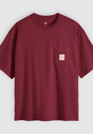 Dunkelrotes T-Shirt mit kurzen Ärmeln und Rundhalsausschnitt, mit einer Brusttasche, die ein kleines weiß-rotes Etikett auf einem einfarbigen Hintergrund zeigt.