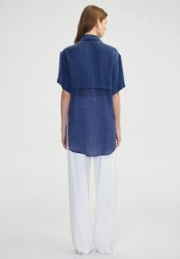 Camisa de manga corta en color navy con dobladillo curvado y detalle trasero transparente, combinada con pantalones blancos holgados, hechos de tejido ligero.