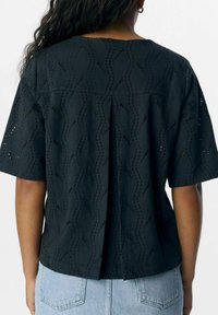 Haut noir à manches courtes avec un motif en œillet ondulé, détail de pli au dos et coupe décontractée. Texture lisse et matière légère.