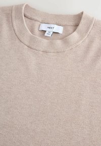Suéter de punto beige con cuello redondo. Textura acanalada y sutil patrón variado. La etiqueta en el cuello dice "NEXT" y tamaño "M".