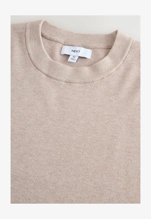 Beige strikket sweater med rund hals. Ribbet tekstur og subtil varieret mønster. Etiketten ved halsen viser "NEXT" og størrelse "M".
