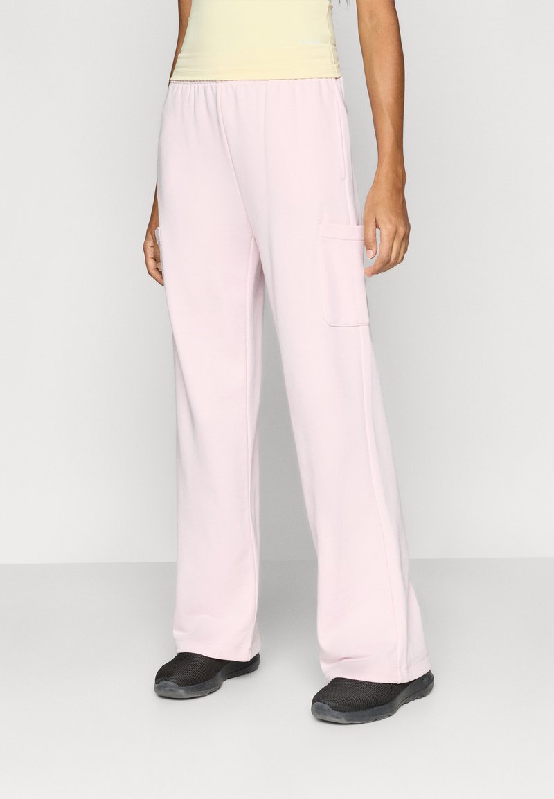 Ροζ ανοιχτό, παντελόνι με φαρδιά μπατζάκια από μαλακό ύφασμα με ελαστική μέση και πλαϊνές τσέπες, συνδυασμένο με μαύρα παπούτσια τύπου slip-on.