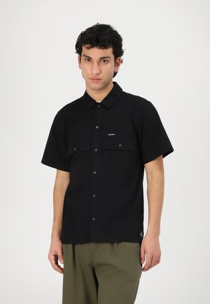 Schwarzes Kurzarmhemd mit Kragen, zwei vorderen Taschen und Druckknöpfen. Weicher Stoff mit glatter Textur und subtilen Branding-Details.