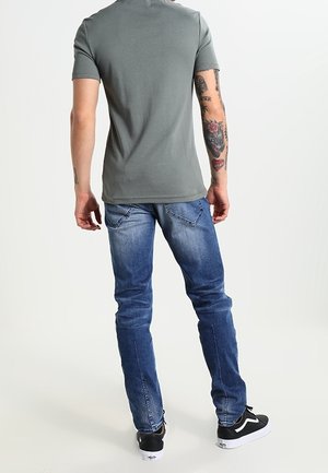 Harmaa istuva t-paita, siniset farkut ja mustat juoksukengät. T-paidassa on lyhyet hihat; farkuissa on haalistunut pinta ja takataskut.