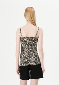 Leopardmønstret topp med tynne stropper, tettsittende design, beige bakgrunn og brune prikker, båret med svarte shorts, glatt stofftekstur.