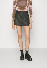 Schwarzer Denim-A-Linien-Rock mit ausgefranstem Saum, kombiniert mit einem gestreiften langärmligen Oberteil und schwarzen Schnürstiefeletten.