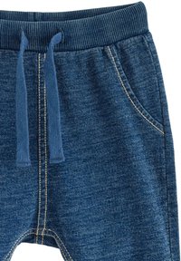 Blå joggers i mjukt, strukturerat tyg med ribbad midja och dragsko. Har sidofickor och kontrasterande sömmar.