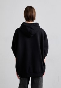 Svart oversized hoodie med en mjuk textur, med en stor huva och korta ärmar, tillsammans med mörkgrå, smalpassande byxor.