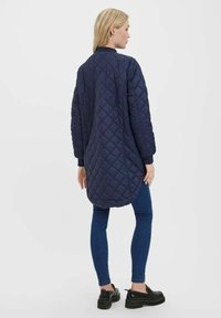 Granatowa pikowana długa kurtka z zaokrąglonym dołem, bocznymi kieszeniami i ściągaczami na rękawach, zestawiona z niebieskimi skinny jeansami i czarnymi platformami.