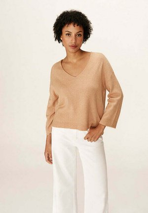 Un pull en maille beige clair, avec un col en V et des manches trois-quarts, associé à un pantalon blanc à jambes larges. Texture lisse et coupe décontractée.