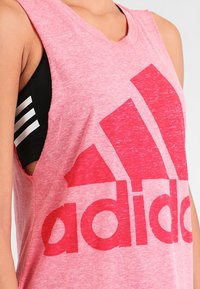 Różowy bezrękawnik Adidas z dużym czerwonym logo, o mi�ękkiej fakturze i delikatnym melanżowym wzorze. Czarny stanik sportowy z widocznymi białymi paskami.