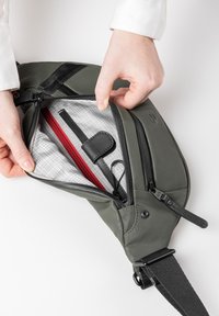 Groene tas met een zwarte band, voorzien van een ritssluiting. Het interieur heeft een grijs ruitpatroon, een rood ritssluitingvak en een zwarte houder.